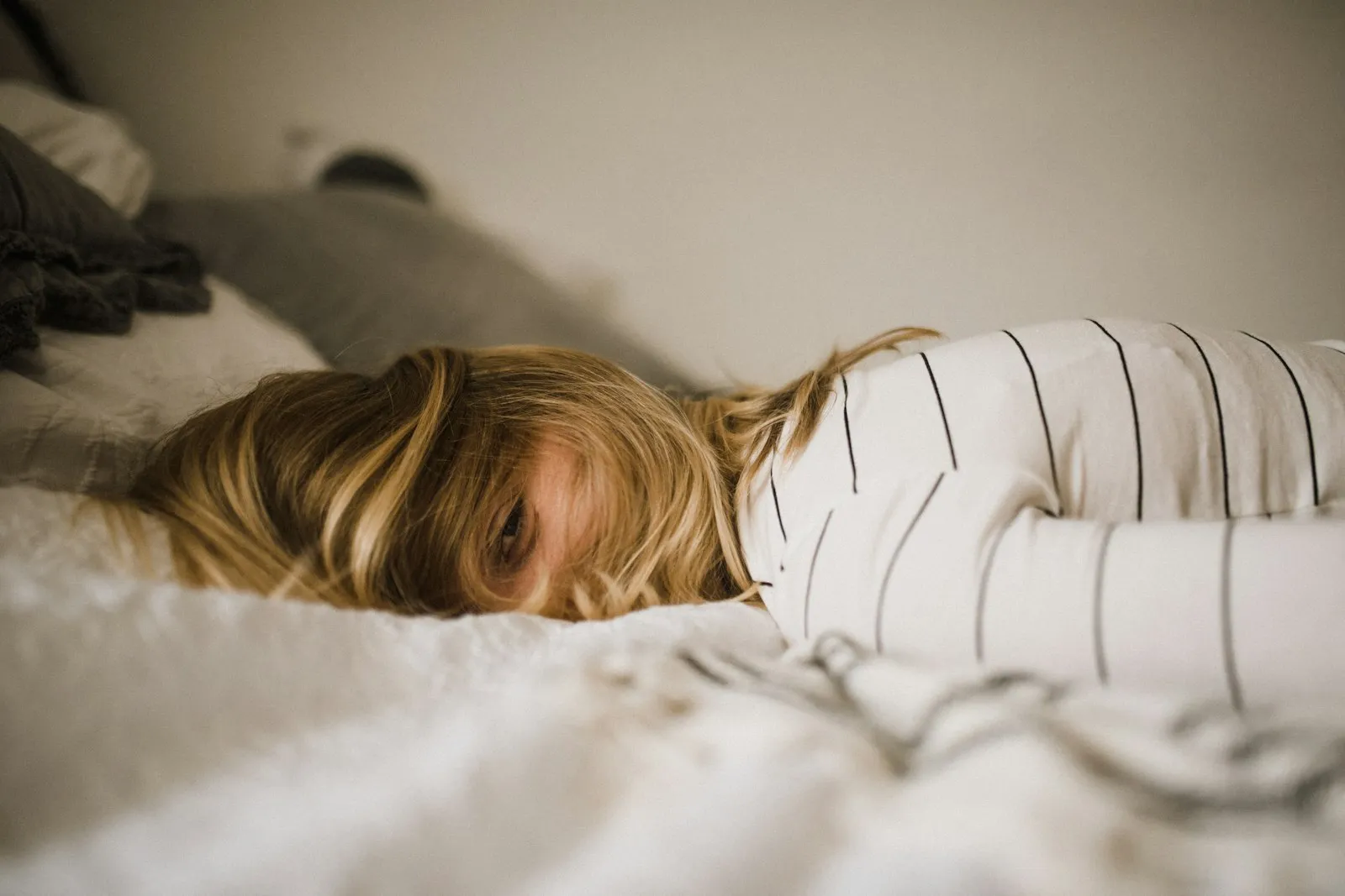 A woman lying on a bed, half her face hidden under her hair, eyes open