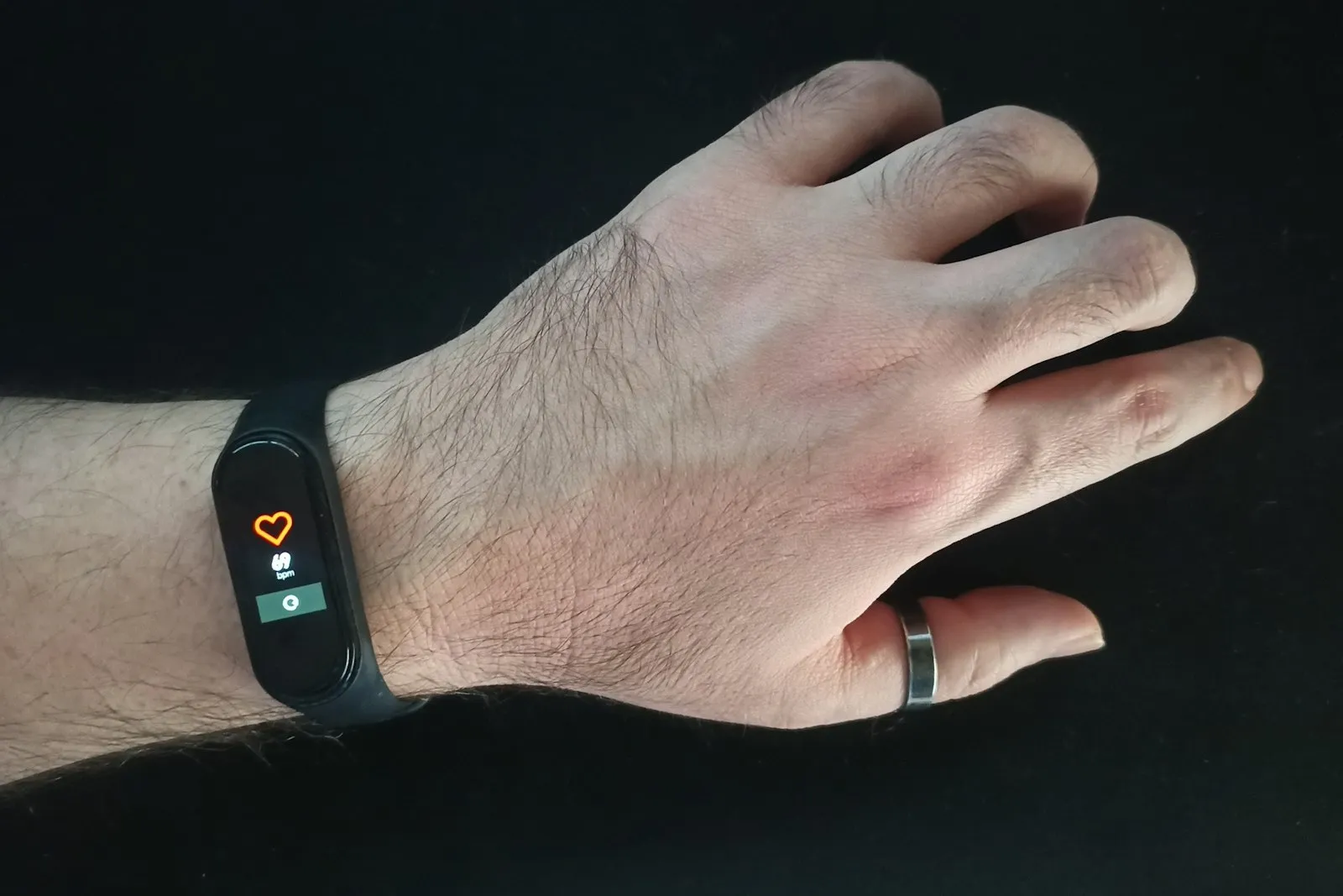 A hand against a dark background wearing a black fitness band on the wrist and a metal ring on one finger