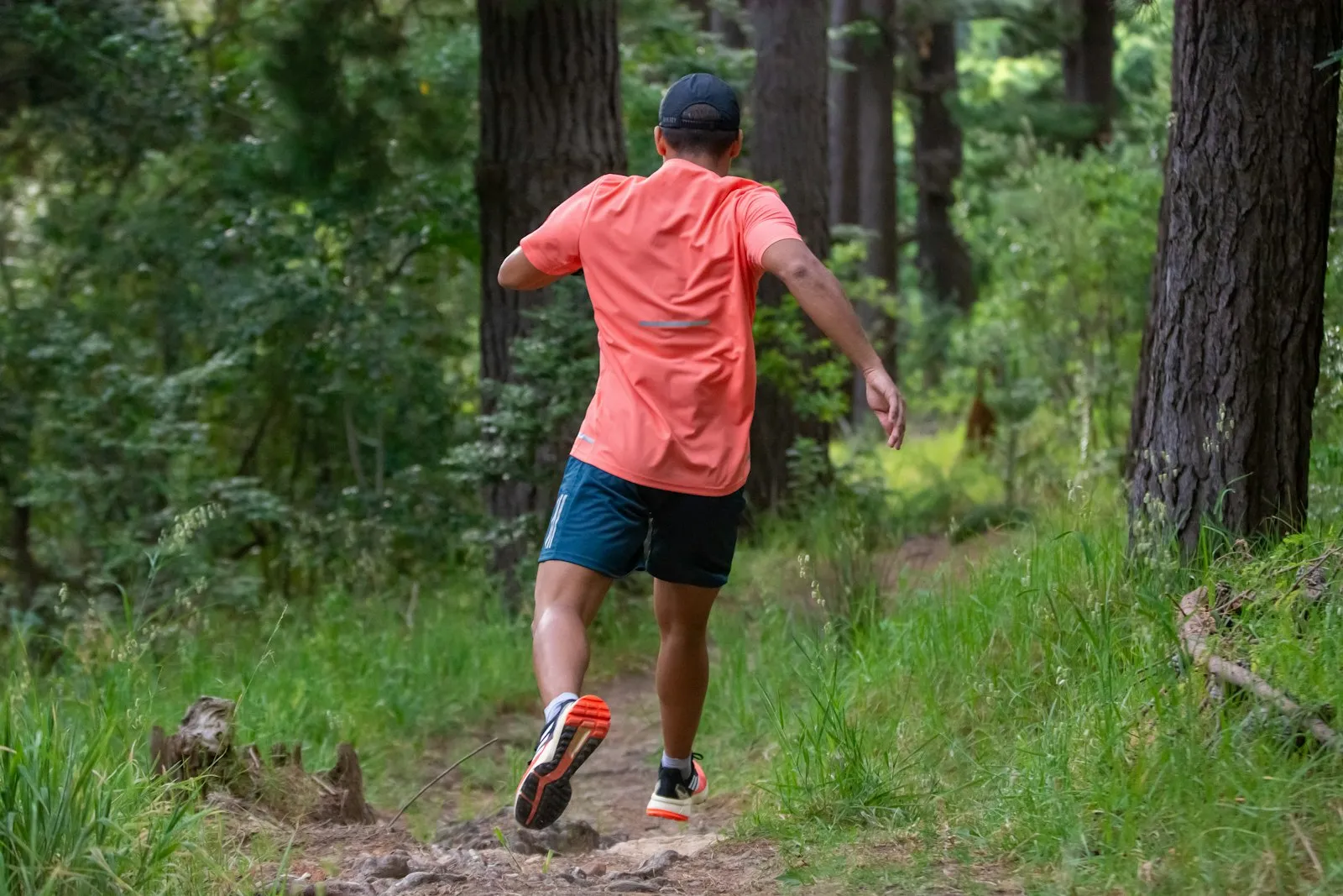 A runner on a wooded trail moving through dappled light