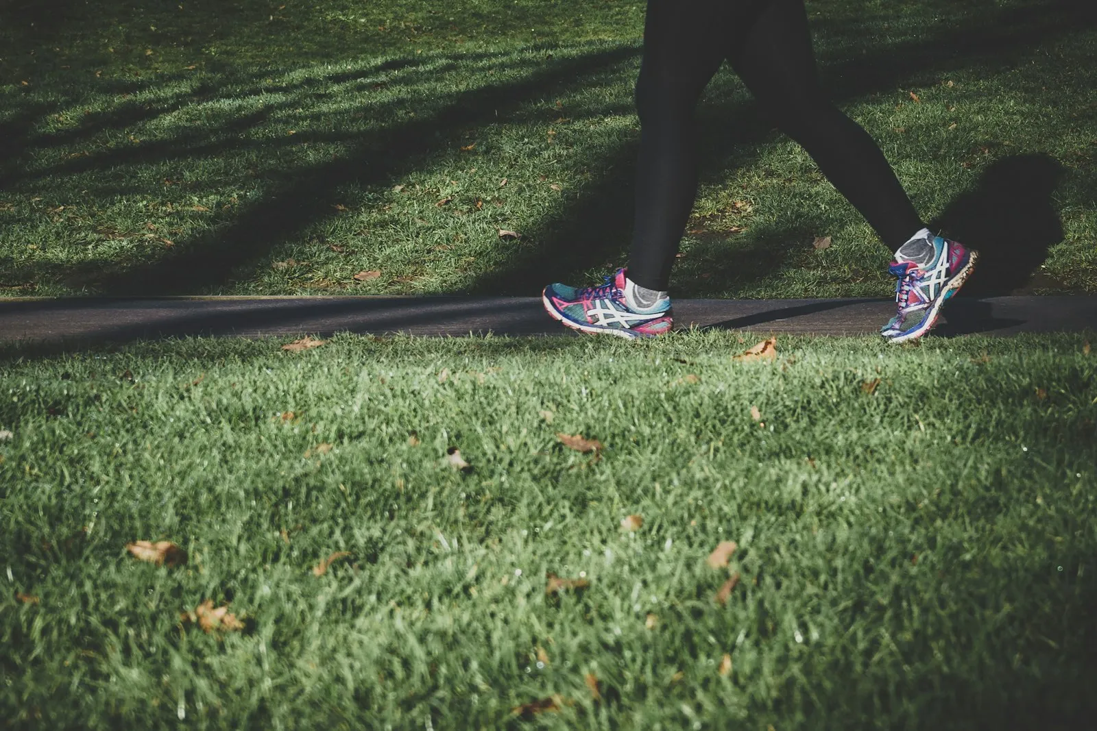 A person walking briskly along a park path, seen from the legs down