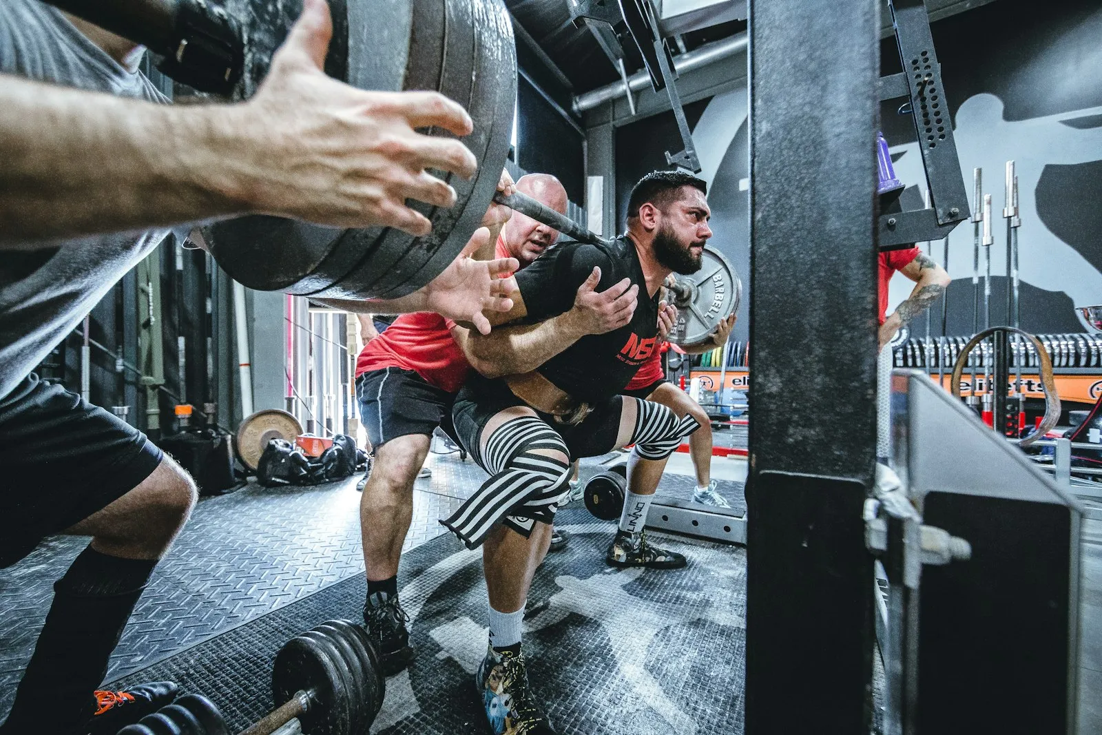 A lifter driving up out of a heavy barbell squat while a training partner spots from behind
